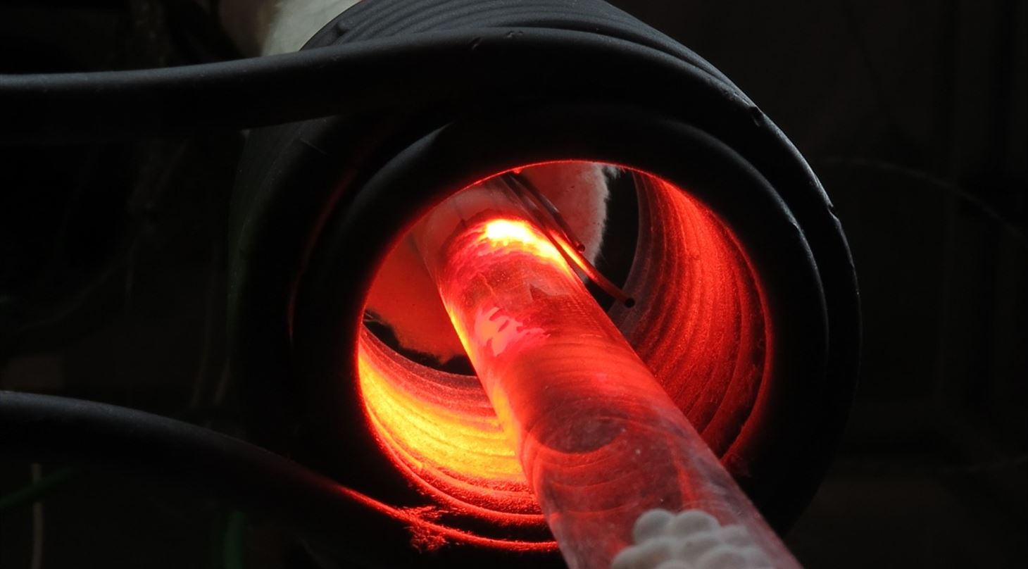 Induction heated tube glowing in dark coil